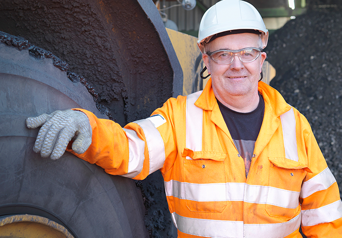 Smiling man in high vis and hard hat looking at camera next to a large vehicle tire